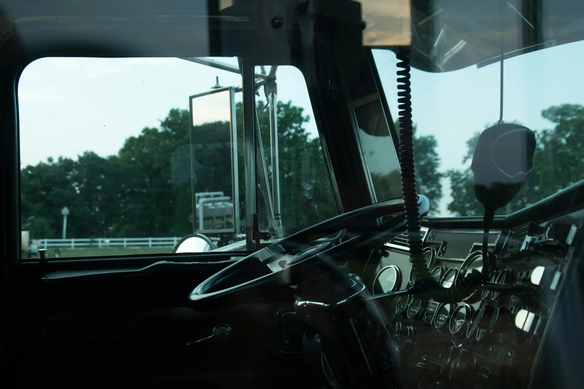 View across a semi truck cab showing the steering wheel, instruments, and road outside