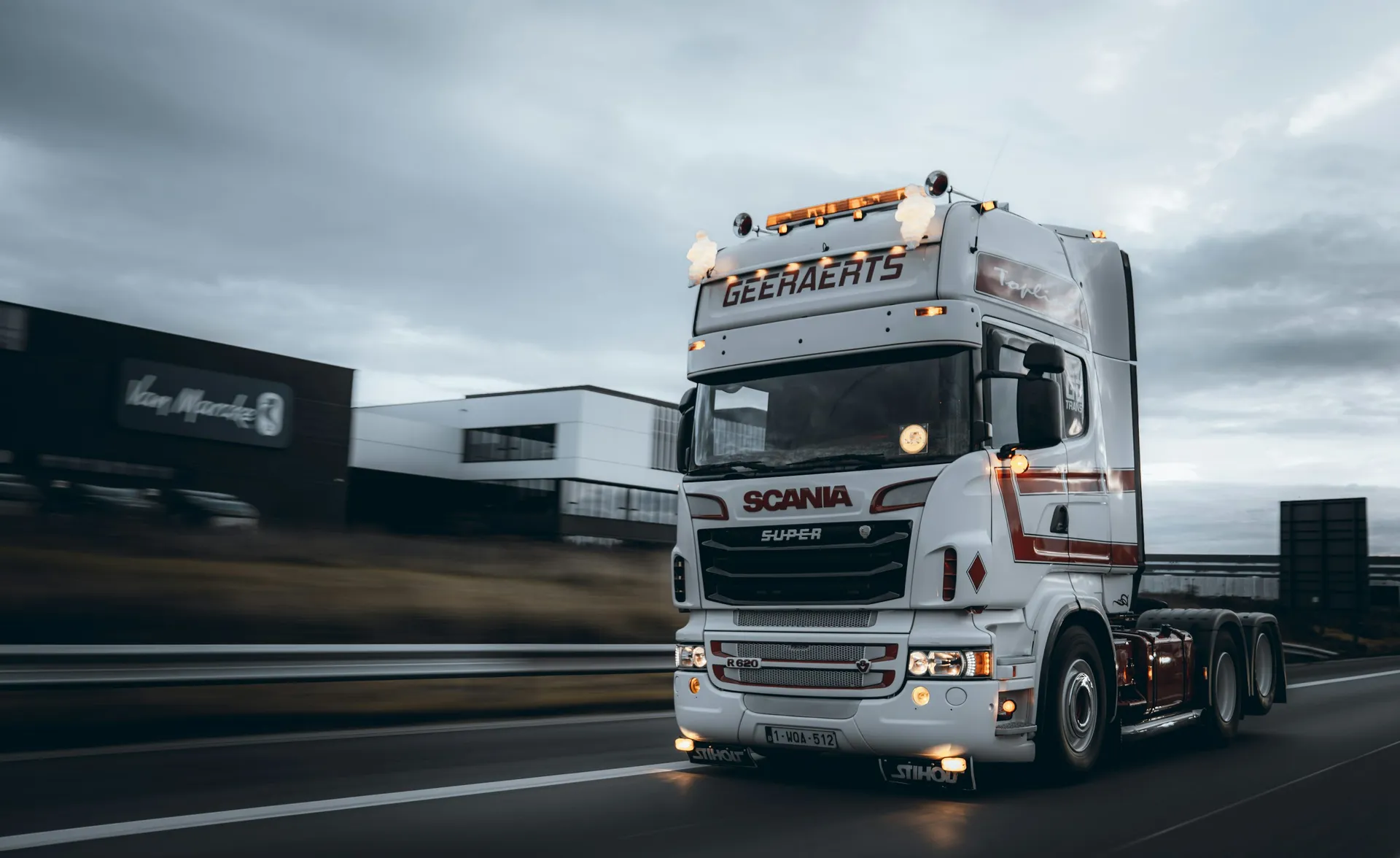 White semi truck moving past industrial buildings on a wet roadway