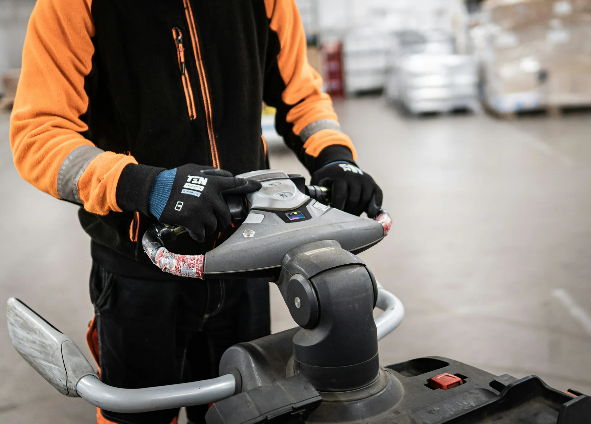 Warehouse worker guiding an electric pallet mover through a distribution floor