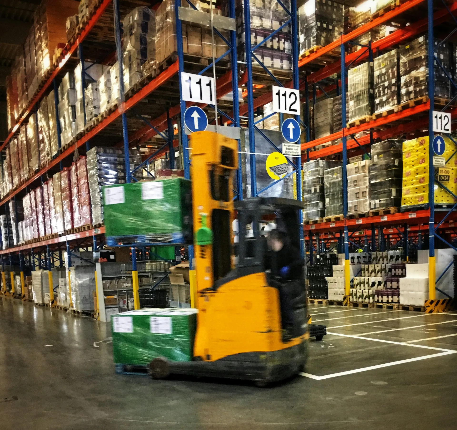 Forklift operator moving wrapped freight through a tall warehouse aisle
